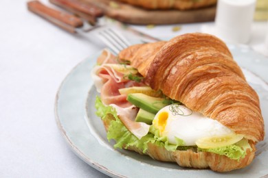 Delicious croissant with prosciutto, avocado and egg on white table, closeup. Space for text