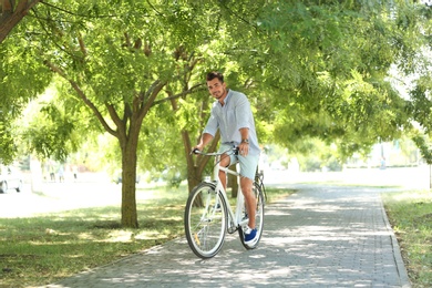 Handsome young hipster man riding bicycle in park