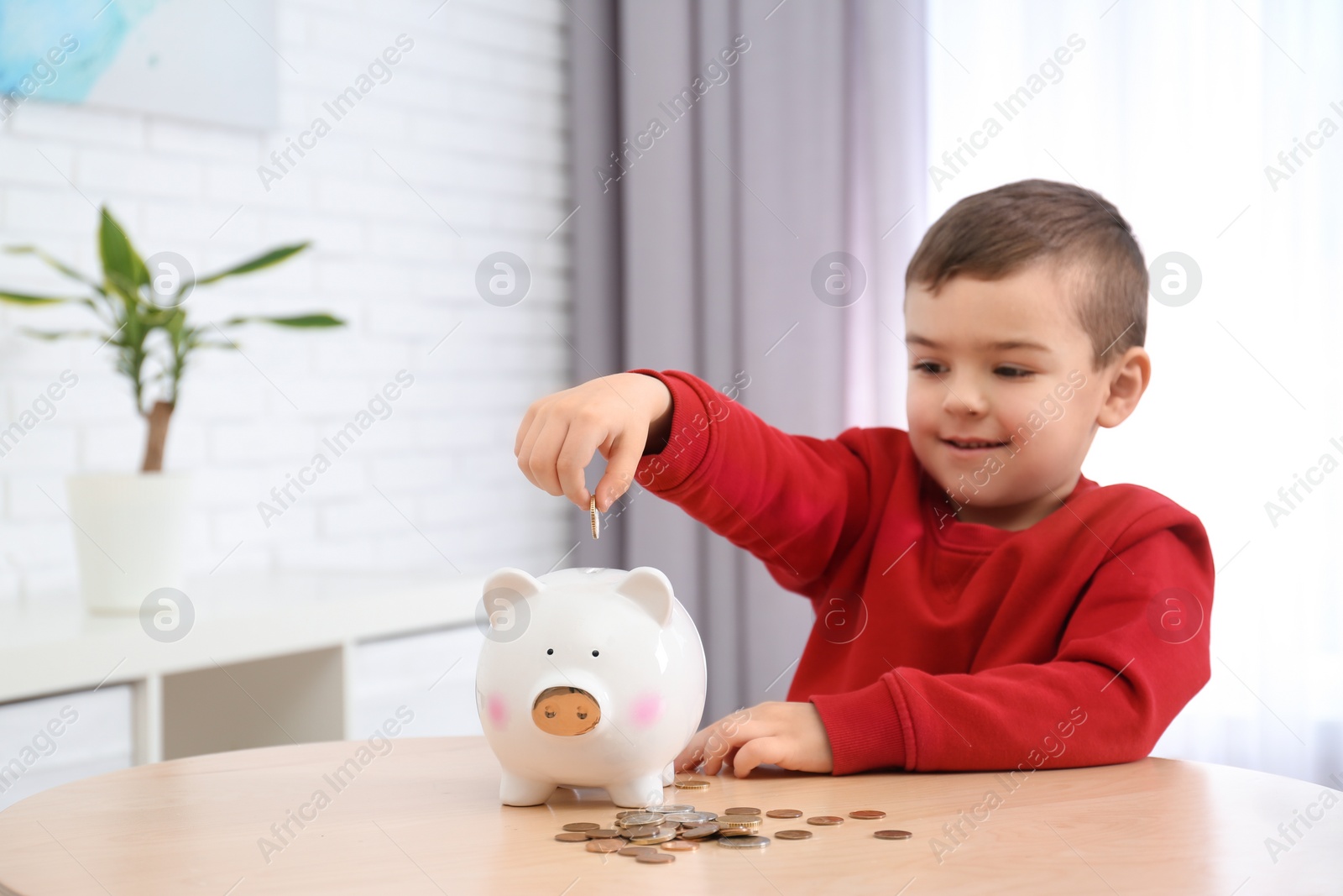 Photo of Little boy with piggy bank and money at home