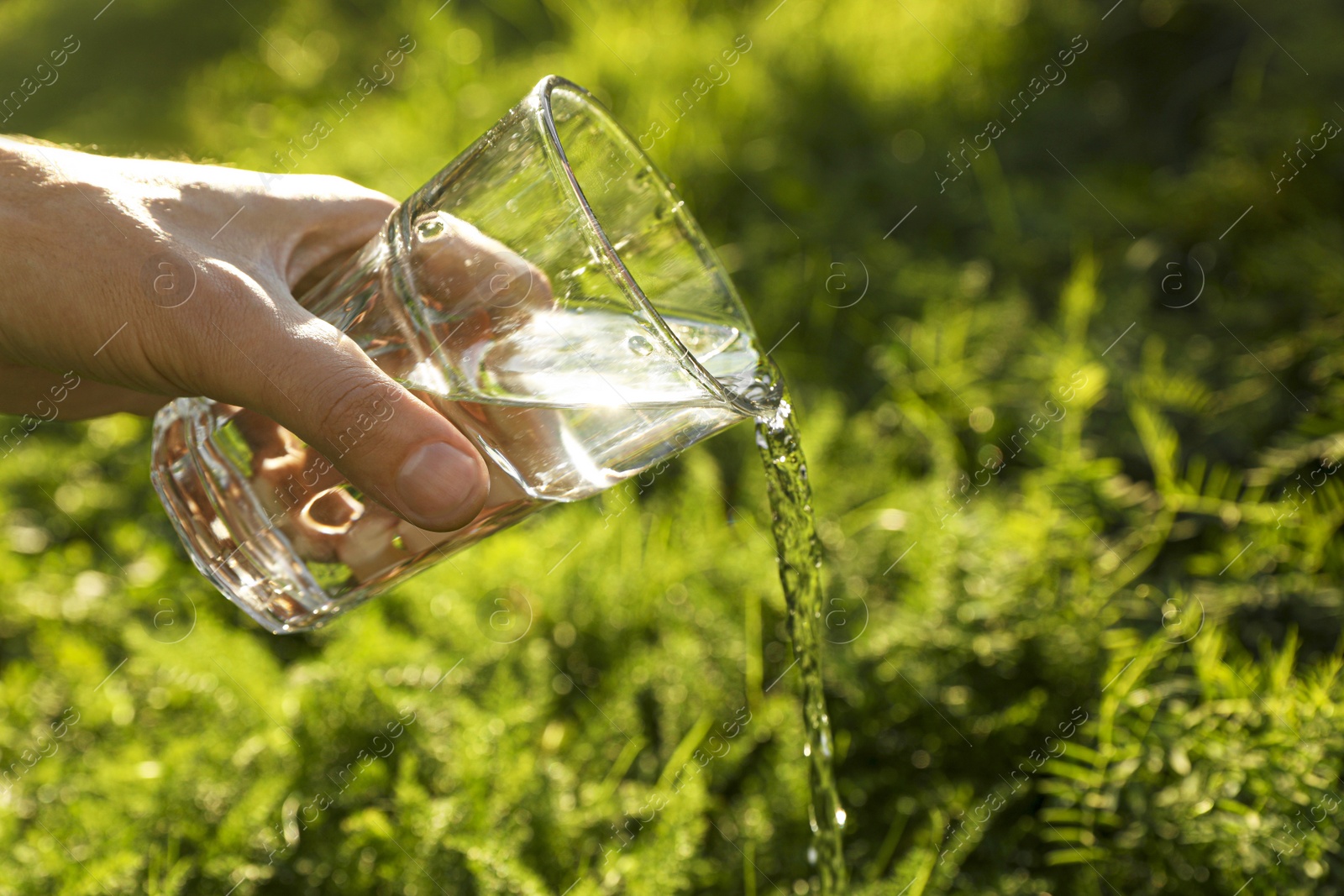 Photo of Man pouring fresh water from glass outdoors, closeup