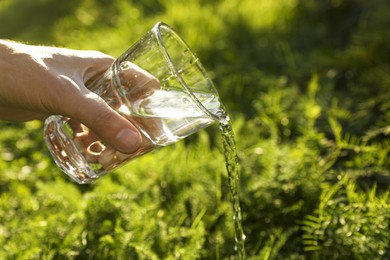 Photo of Man pouring fresh water from glass outdoors, closeup