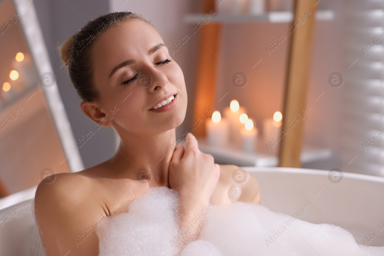 Photo of Beautiful woman taking bath in tub with foam indoors. Space for text