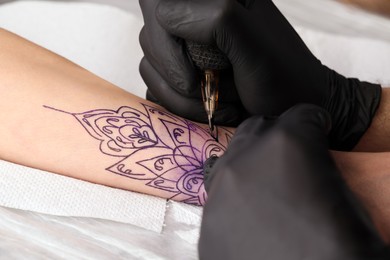 Photo of Professional artist making tattoo on hand at table, closeup