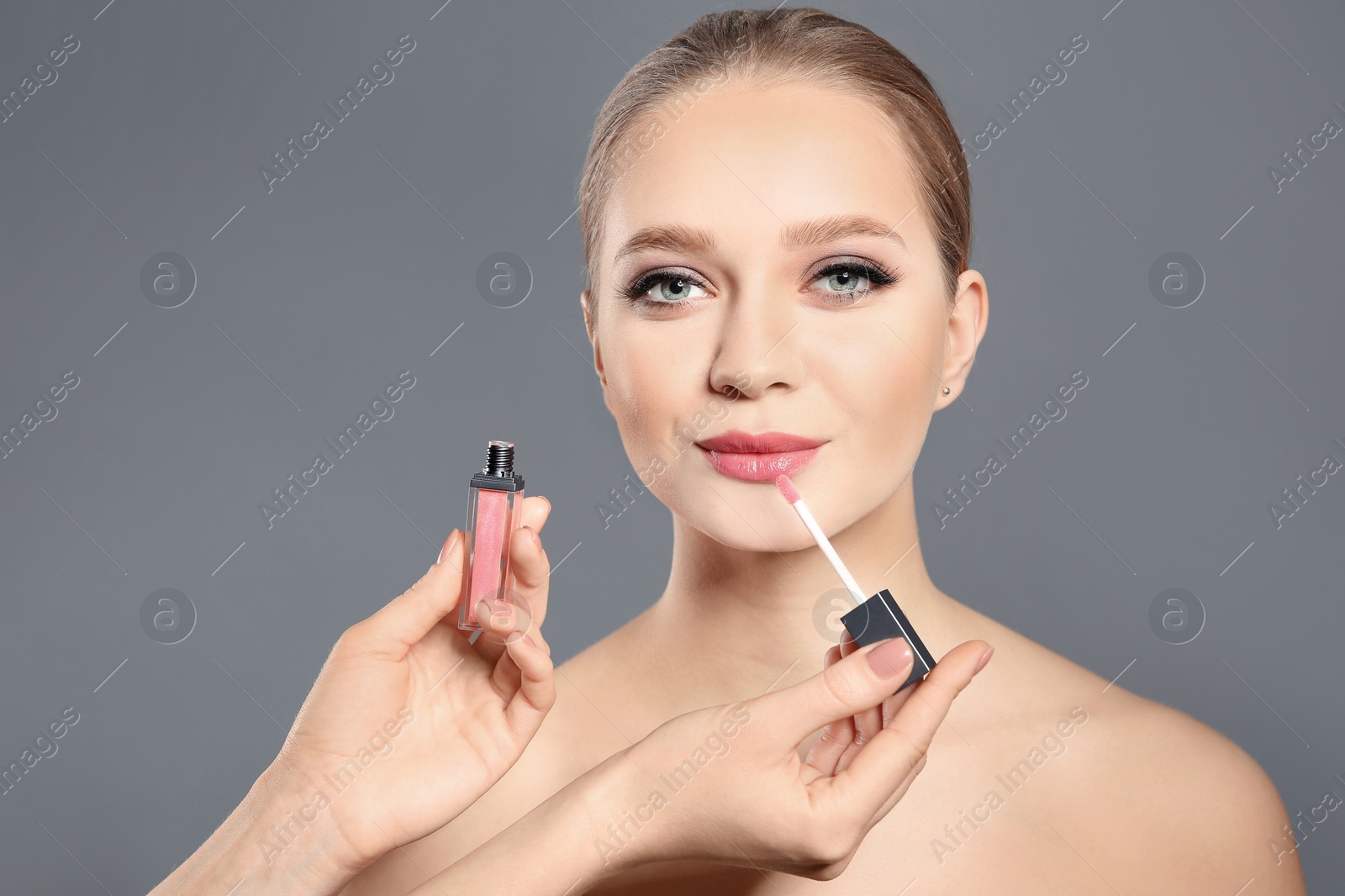 Photo of Artist applying makeup onto woman's face on light grey background