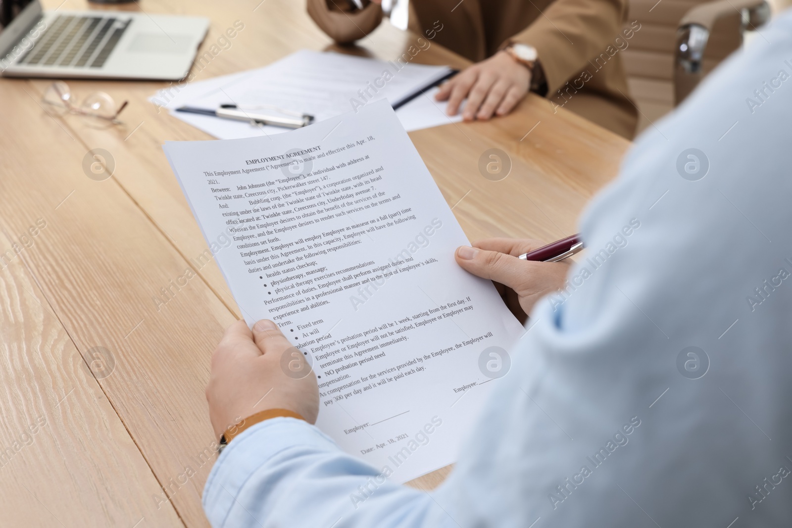 Photo of Man reading employment agreement at table in office, closeup. Signing contract