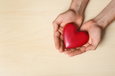 Young man holding red heart on light wooden background, top view with space for text. Donation concept