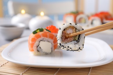 Taking tasty sushi roll from plate with chopsticks on table, closeup