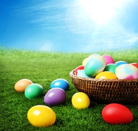 Wicker basket with Easter eggs on green grass outdoors