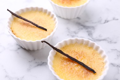 Delicious creme brulee in bowls and vanilla pods on white marble table, closeup