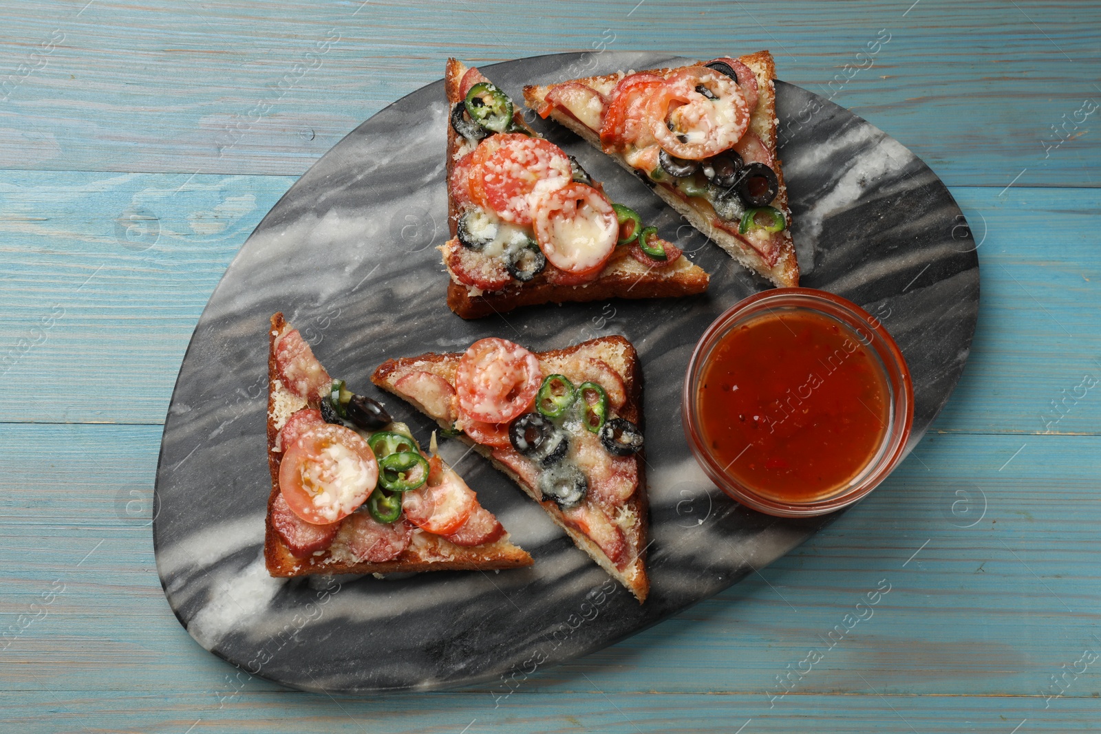 Photo of Tasty pizza toasts and sauce on light blue wooden table, top view