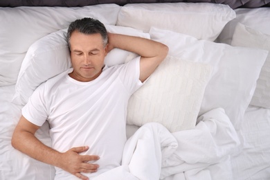 Photo of Man sleeping on comfortable pillow in bed at home, top view