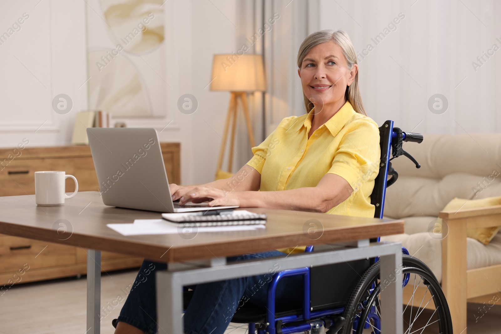 Photo of Woman in wheelchair using laptop at table in home office