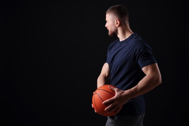 Photo of Athletic young man with basketball ball on black background. Space for text