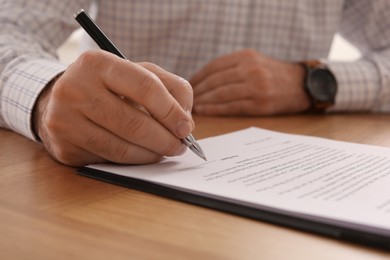 Photo of Businessman signing contract at wooden table, closeup of hands