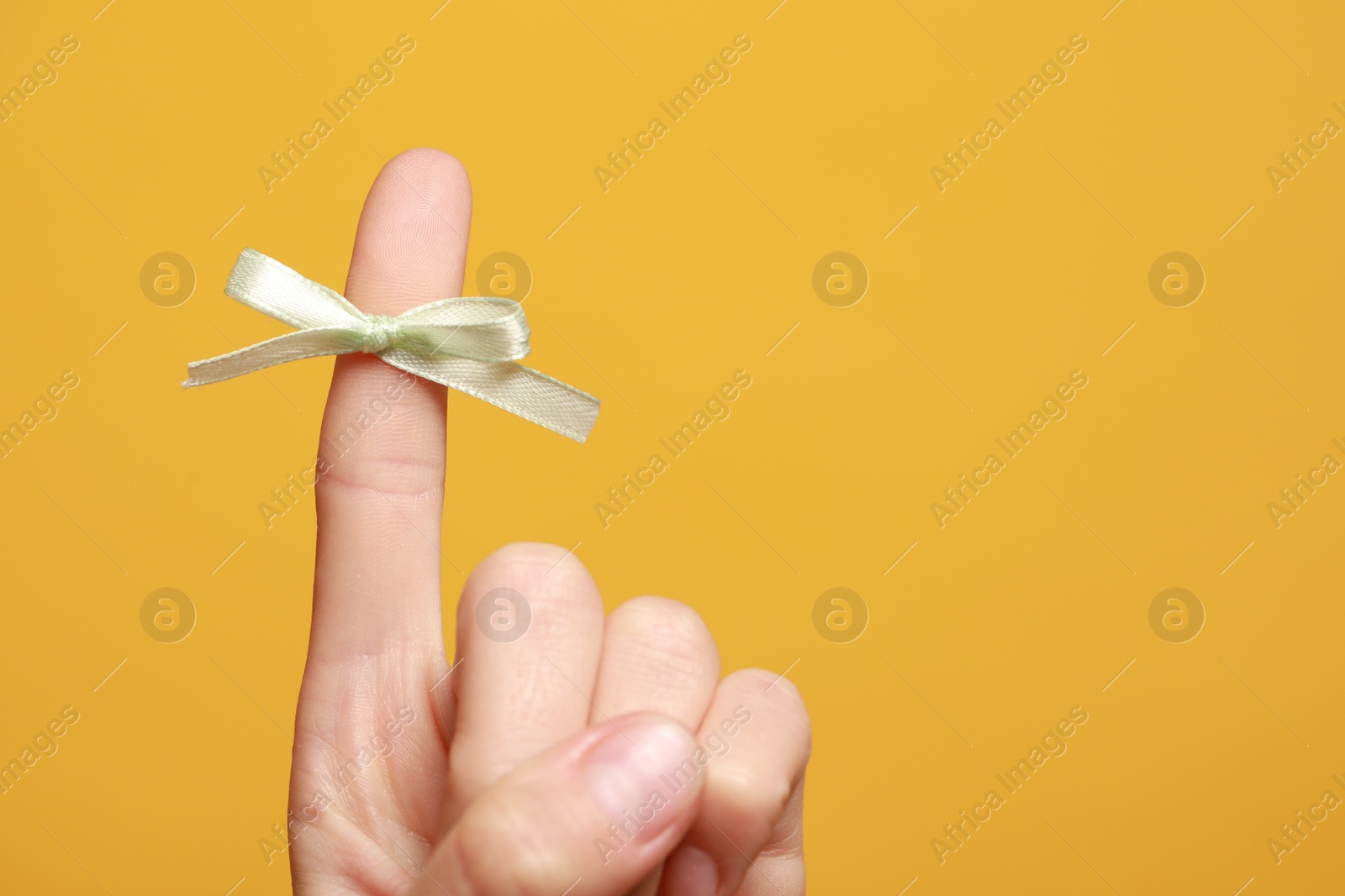 Photo of Woman showing index finger with tied bow as reminder on orange background, closeup. Space for text