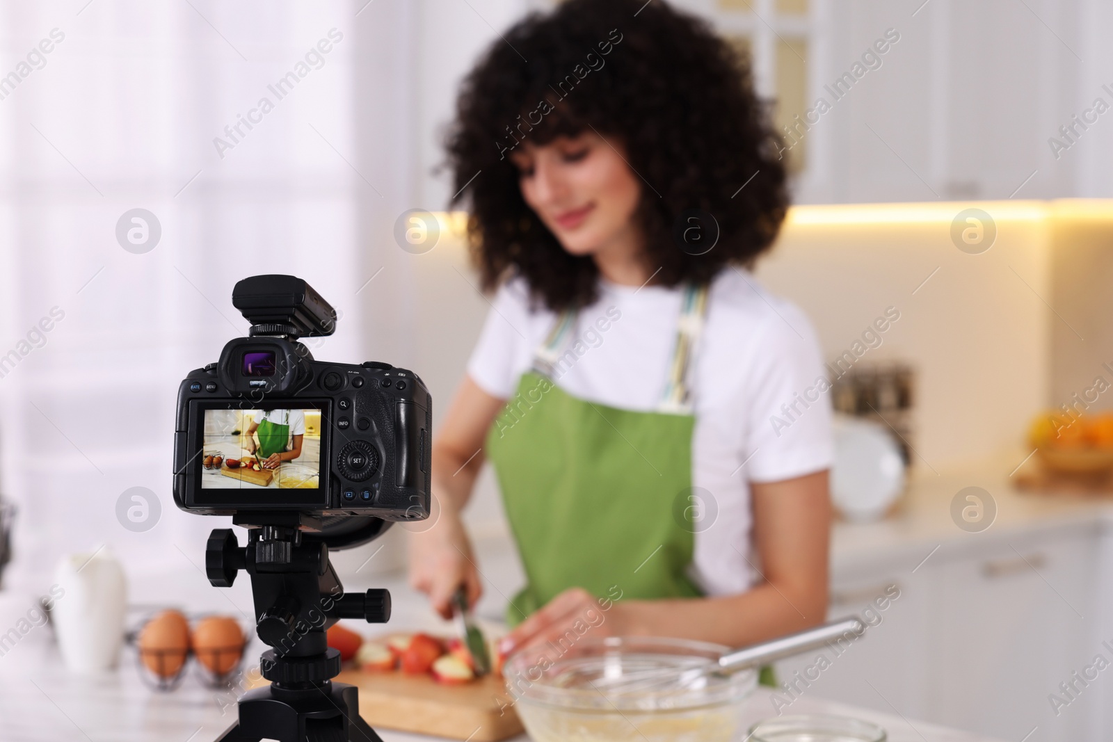 Photo of Food blogger cooking while recording video in kitchen, focus on camera