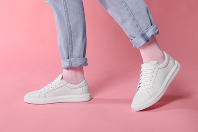 Woman wearing stylish white sneakers on pink background, closeup