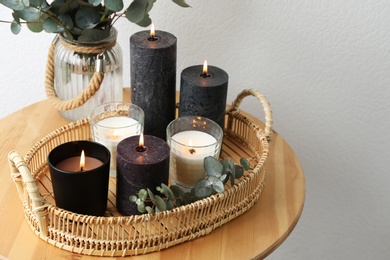 Tray with burning candles and green branches on table at white wall, space for text