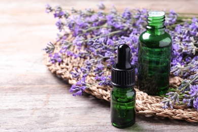 Photo of Bottles of essential oil and lavender flowers on wooden table. Space for text