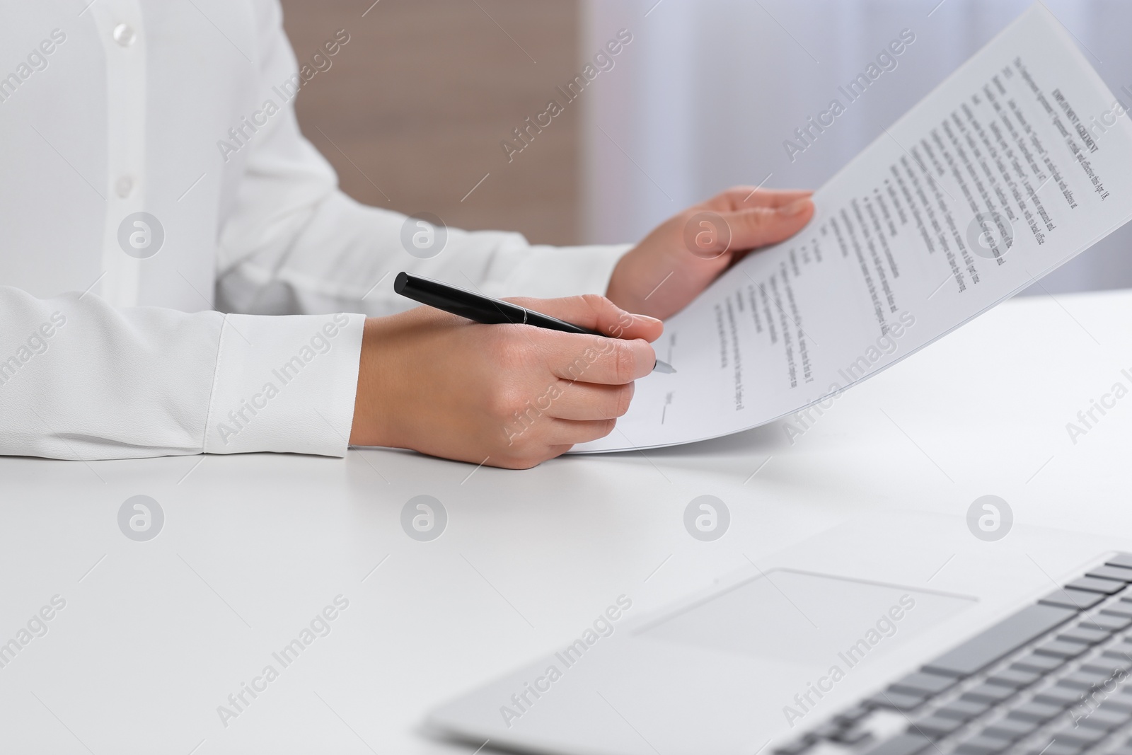 Photo of Businesswoman signing contract at white table in office, closeup of hands