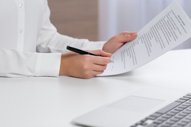 Photo of Businesswoman signing contract at white table in office, closeup of hands