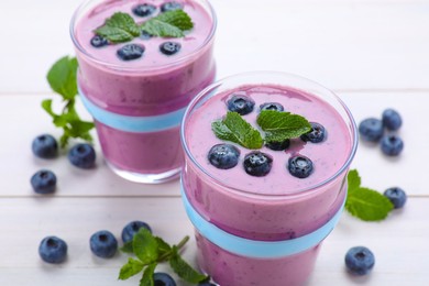 Photo of Glasses of blueberry smoothie with mint and fresh berries on white wooden table, closeup
