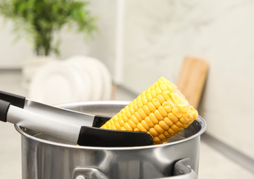Photo of Taking boiled corn from pot with tongs in kitchen