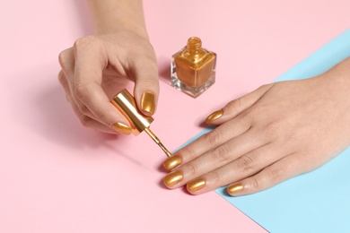 Woman painting nails with golden polish on color background, closeup