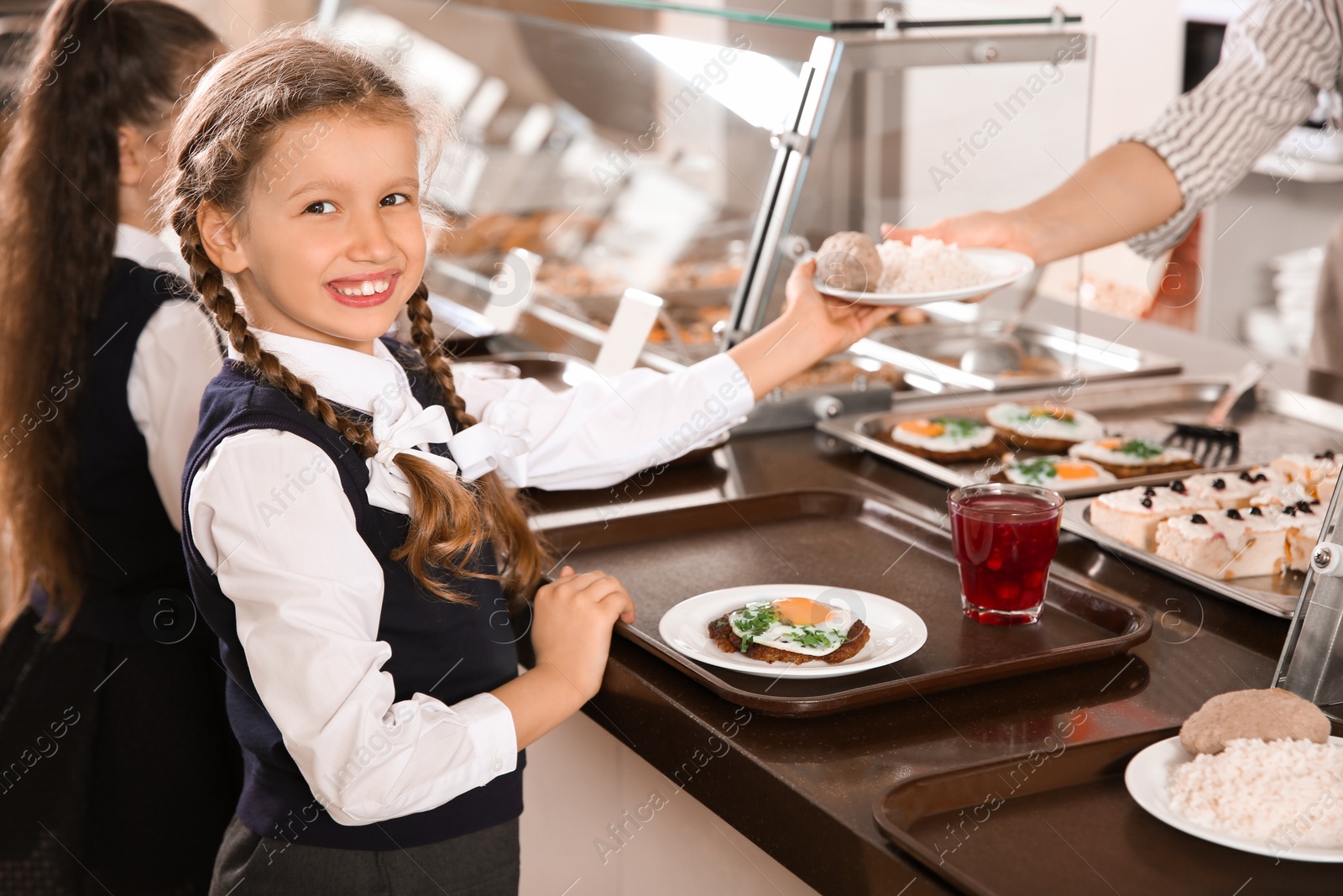 Photo of Woman giving plate with healthy food to girl in school canteen