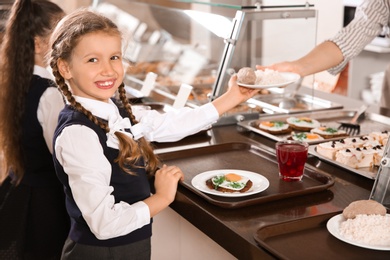 Woman giving plate with healthy food to girl in school canteen