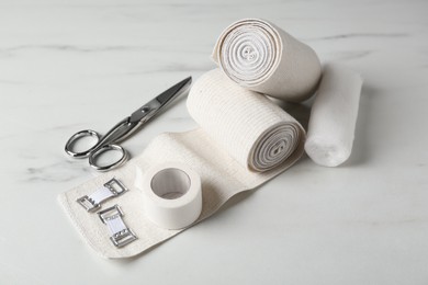 Photo of Medical bandage rolls, sticking plaster and scissors on white wooden table