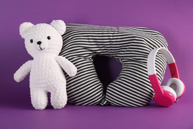 Photo of Striped travel pillow, toy bear and headphones on violet background