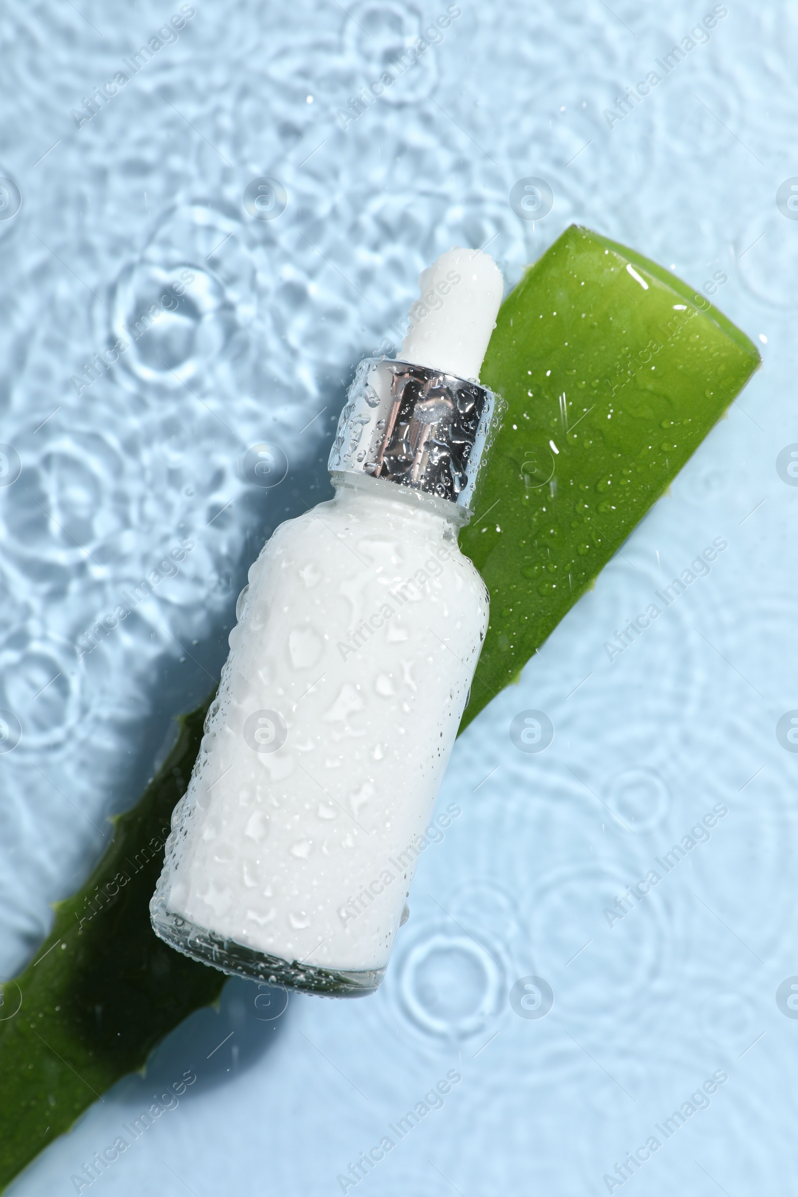 Photo of Bottle of cosmetic product and aloe leaf in water on light blue background, flat lay