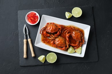 Delicious boiled crabs with sauce and lime served on black textured table, top view
