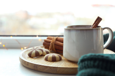 Cup of delicious mulled wine and cookies on window sill indoors. Winter drink