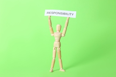Photo of Wooden mannequin holding card with word Responsibility on light green background