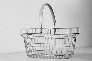 Empty metal shopping basket on light wooden table against white background