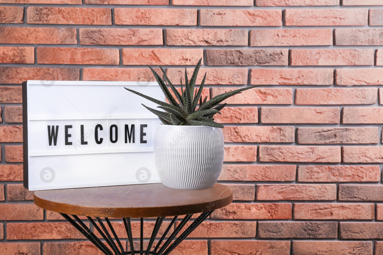 Photo of Lightbox with word Welcome near houseplant on wooden table, space for text