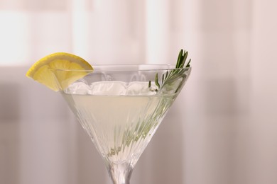 Elegant martini glass with fresh cocktail, rosemary and lemon slice on blurred background, closeup