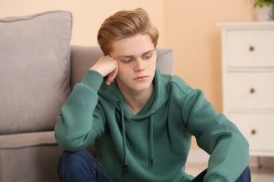 Photo of Upset teenage boy sitting alone in room