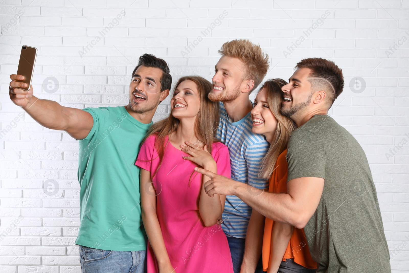 Photo of Happy young people taking selfie near white brick wall