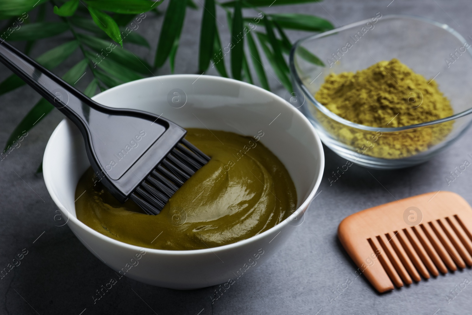 Photo of Bowl of henna cream, brush and comb on light grey table, closeup. Natural hair coloring