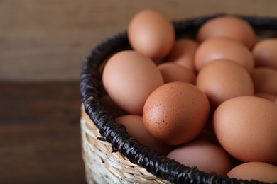 Photo of Raw chicken eggs in wicker basket on wooden table, closeup. Space for text
