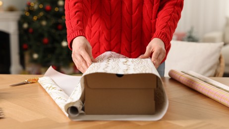 Photo of Woman wrapping Christmas gift at wooden table indoors, closeup