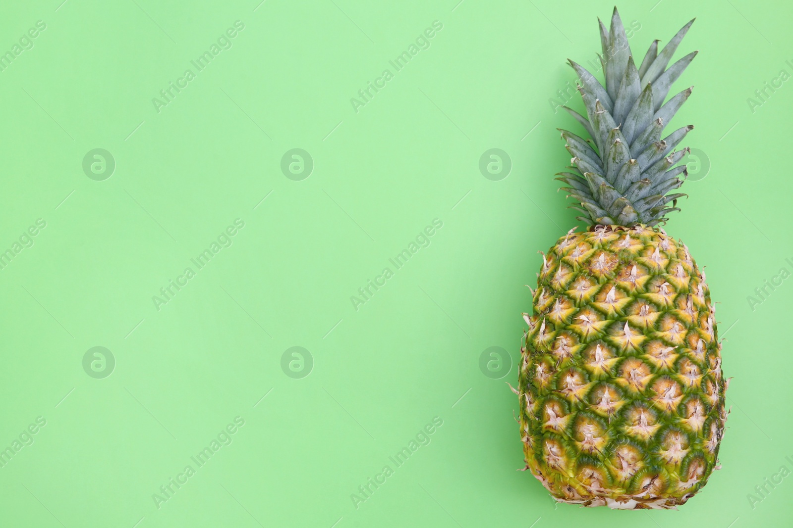 Photo of Whole ripe pineapple on light green background, top view. Space for text