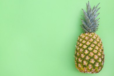 Photo of Whole ripe pineapple on light green background, top view. Space for text
