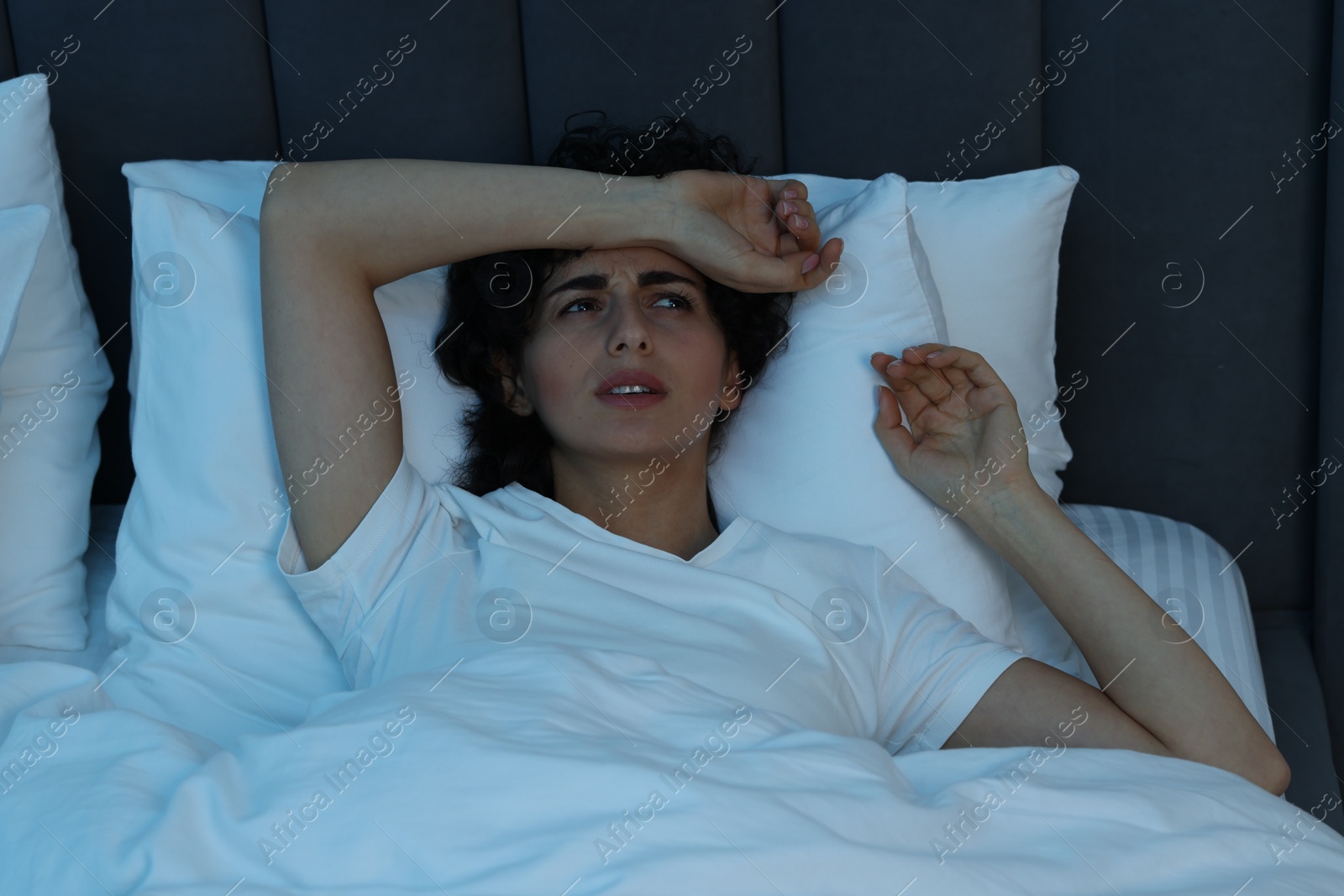 Photo of Young woman suffering from headache in bed at night