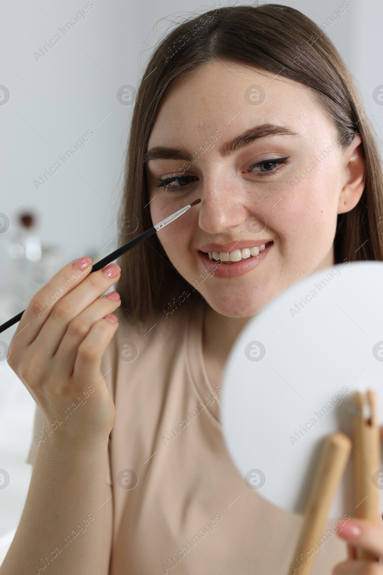 Photo of Smiling woman drawing freckles with brush indoors