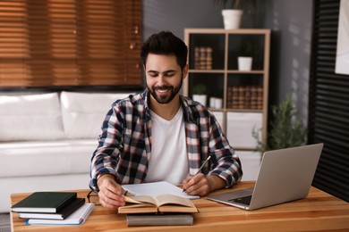 Photo of Young man writing down notes during webinar at table in room