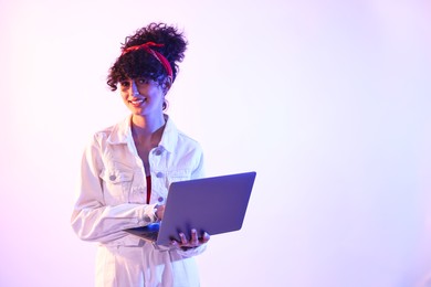 Photo of Beautiful young woman with laptop on color background in neon lights. Space for text